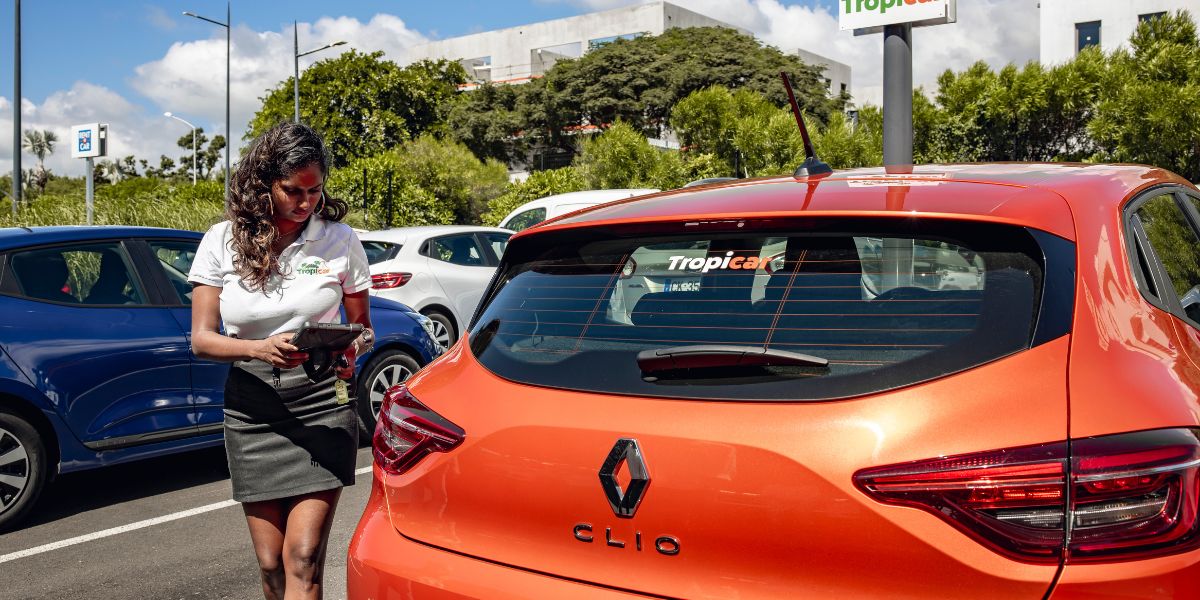 Une hôtesse Tropicar souriante et professionnelle effectue un état des lieux minutieux d'une Renault Clio sur le parking de l'aéroport Roland Garros à La Réunion